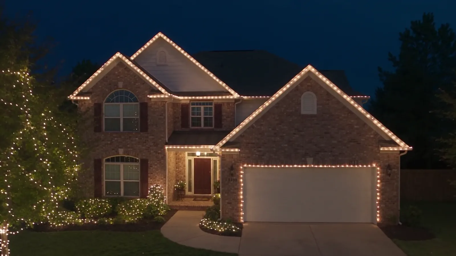 Two-story brick home glowing with warm white Christmas lights